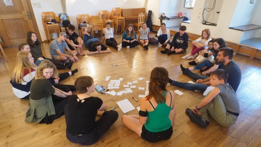 Around twenty participants is sitting in a circle on the ground working on the play